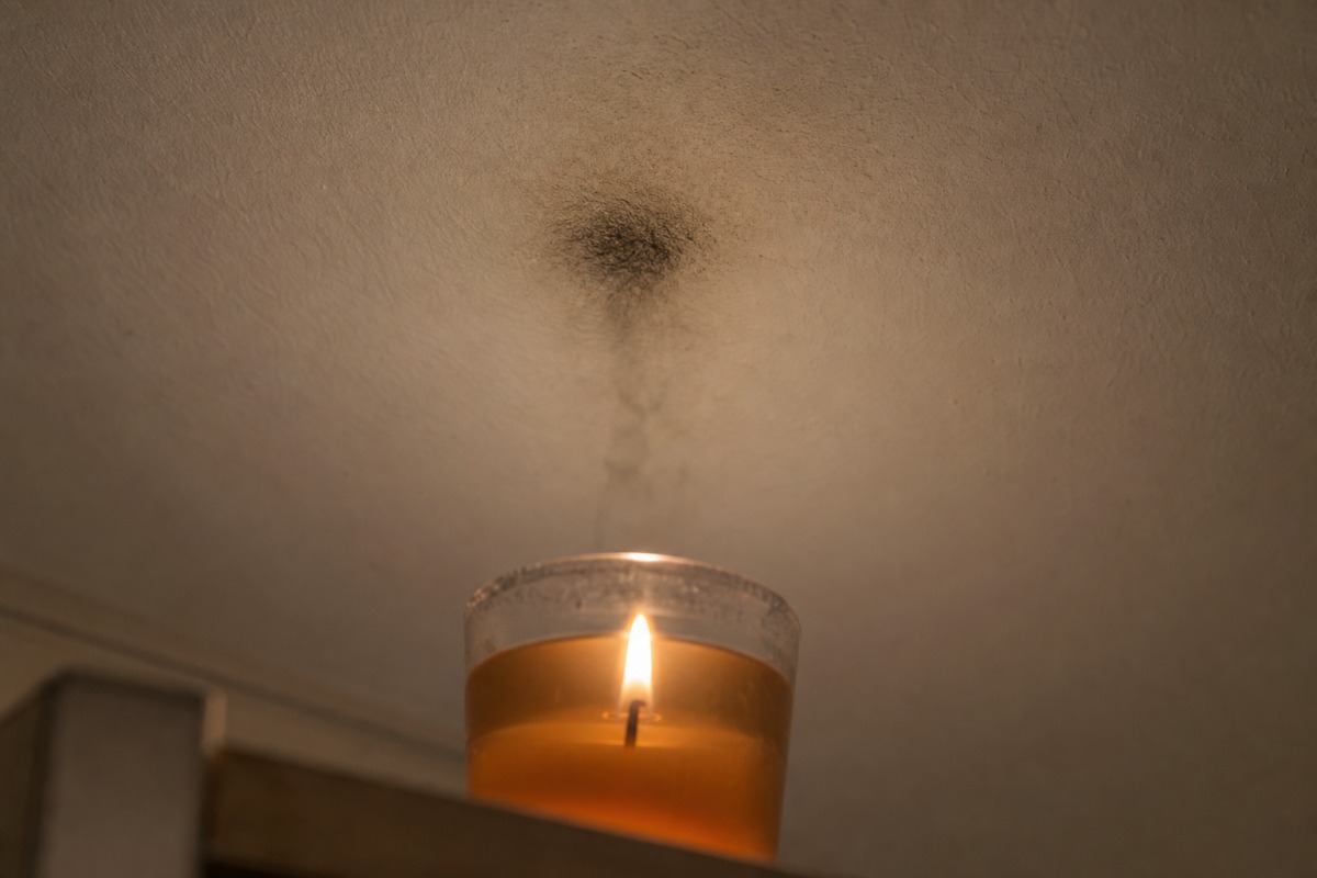 Tmavá stopa sazí na bílém stropě přímo nad hořící gelovou svíčkou ve skleněné sklenici