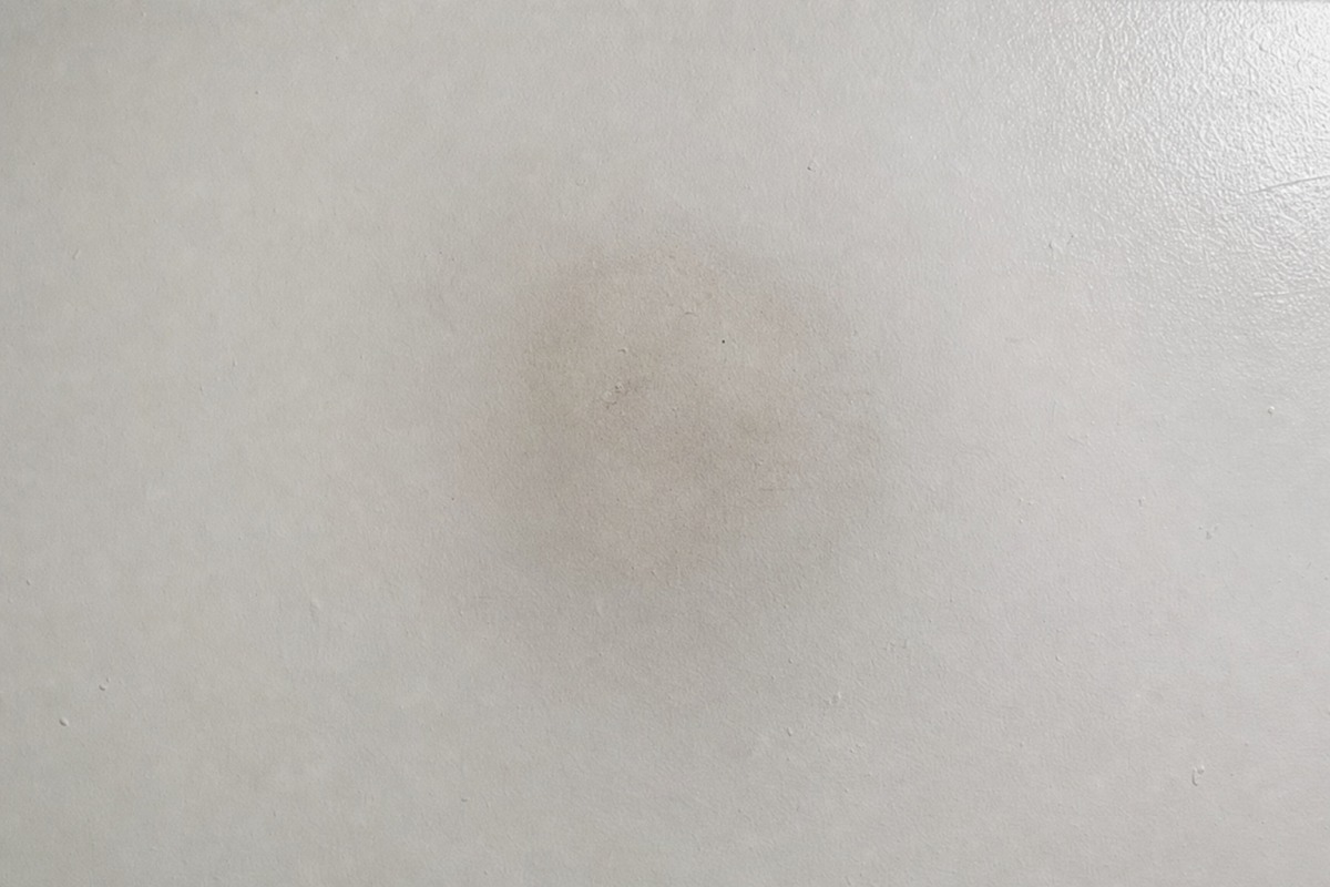 Jemný šedý stín sazí na bílém stropě nad místem, kde stála parafínová svíčka